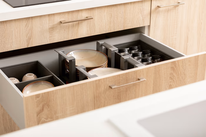 Deep kitchen drawer pulled open, fitted with adjustable dividers and pegs holding stacked plates and bowls upright