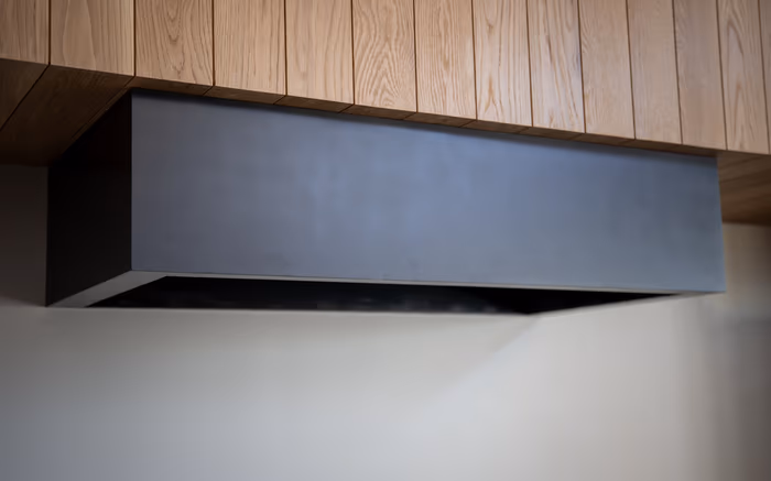 Stainless hood insert built into a timber-clad enclosure above a cooktop, with the duct chase running up behind the cladding