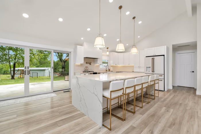 Long kitchen island with a mitred waterfall end panel and four stools tucked under a seating overhang, with pendant lights above